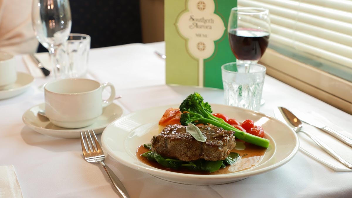 Meal of steak and vegetables served in dining carriage on vintage rail journey.