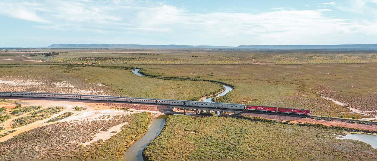 The Ghan train in a vast arid landscape with the Flinders Ranges in the background.
