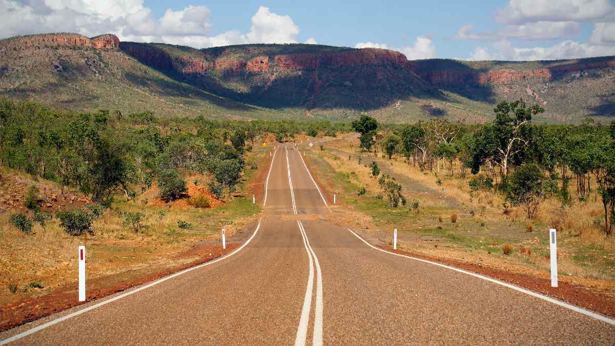 long desert road with shrubs and cliffs in background