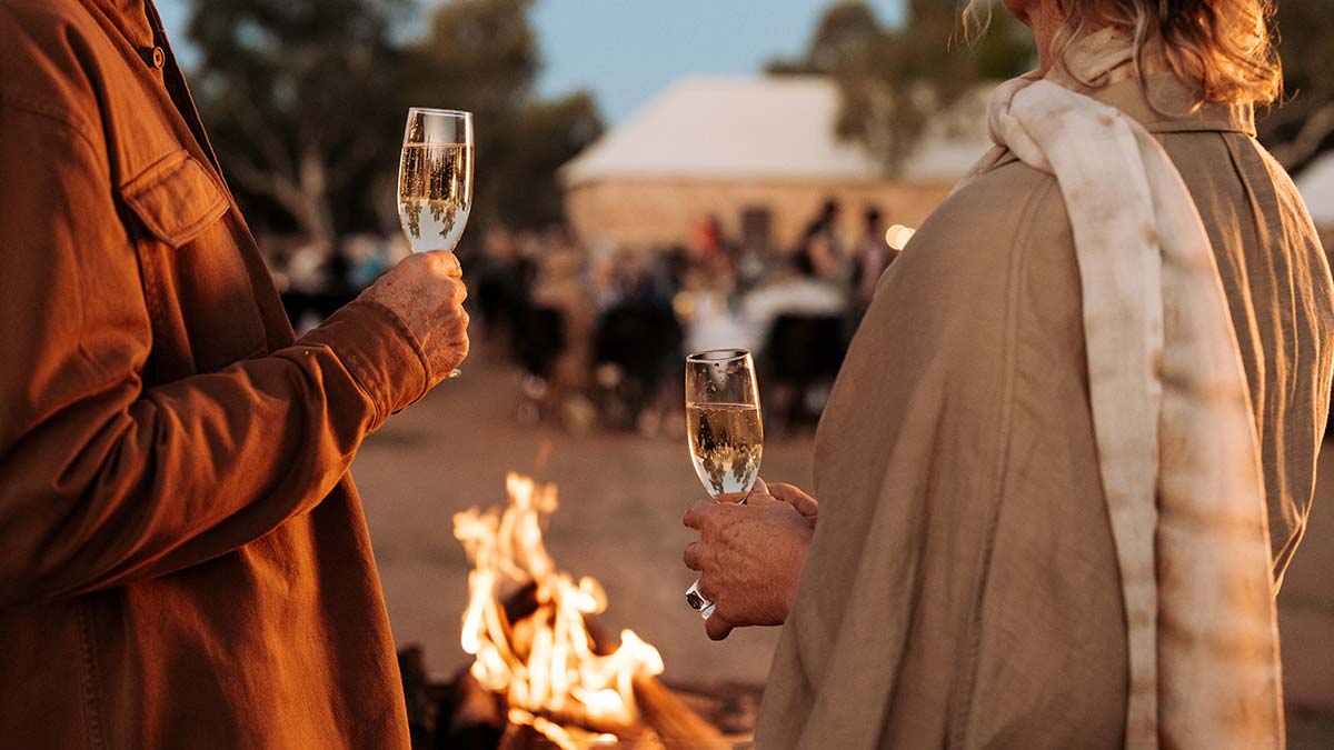 A couple enjoy a glasses of wine next to a campfire at Telegraph Station in Alice Springs, Australia.