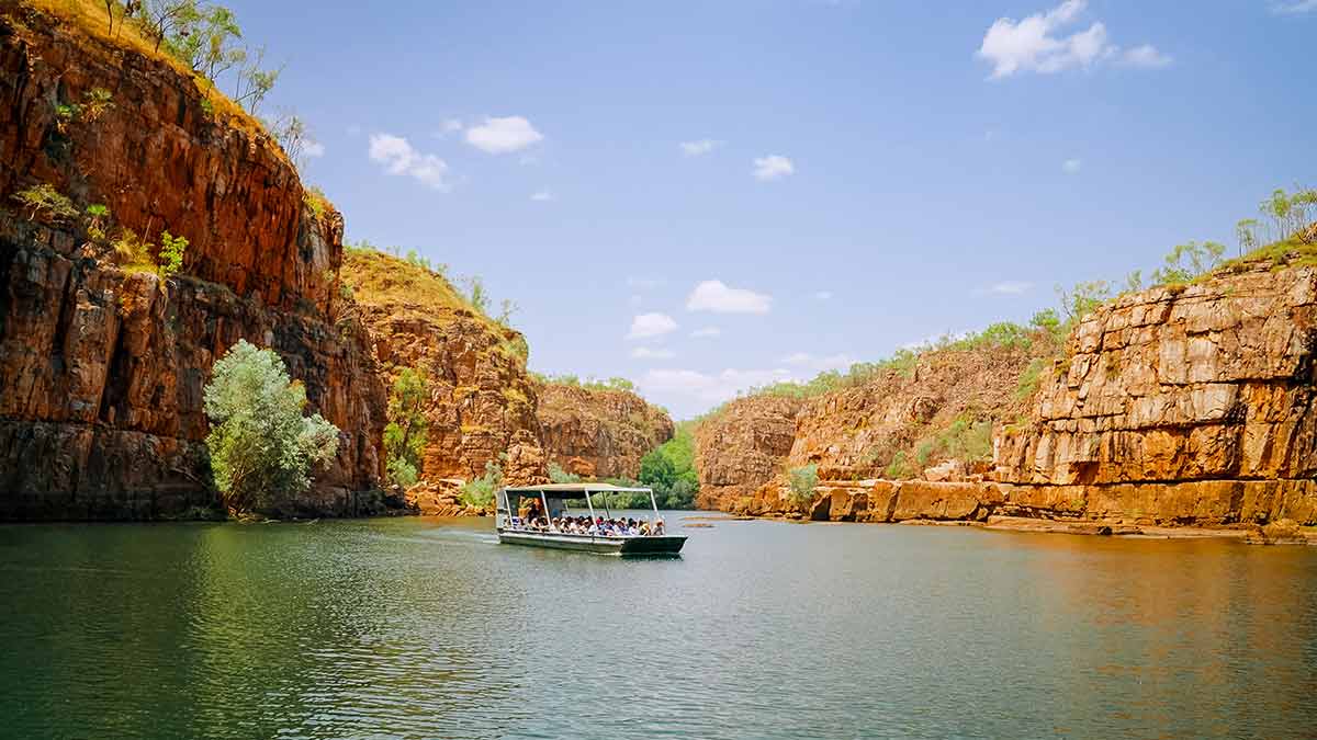 People aboard a boat cruise along a river flanked by red cliffs in Katherine Gorge.
