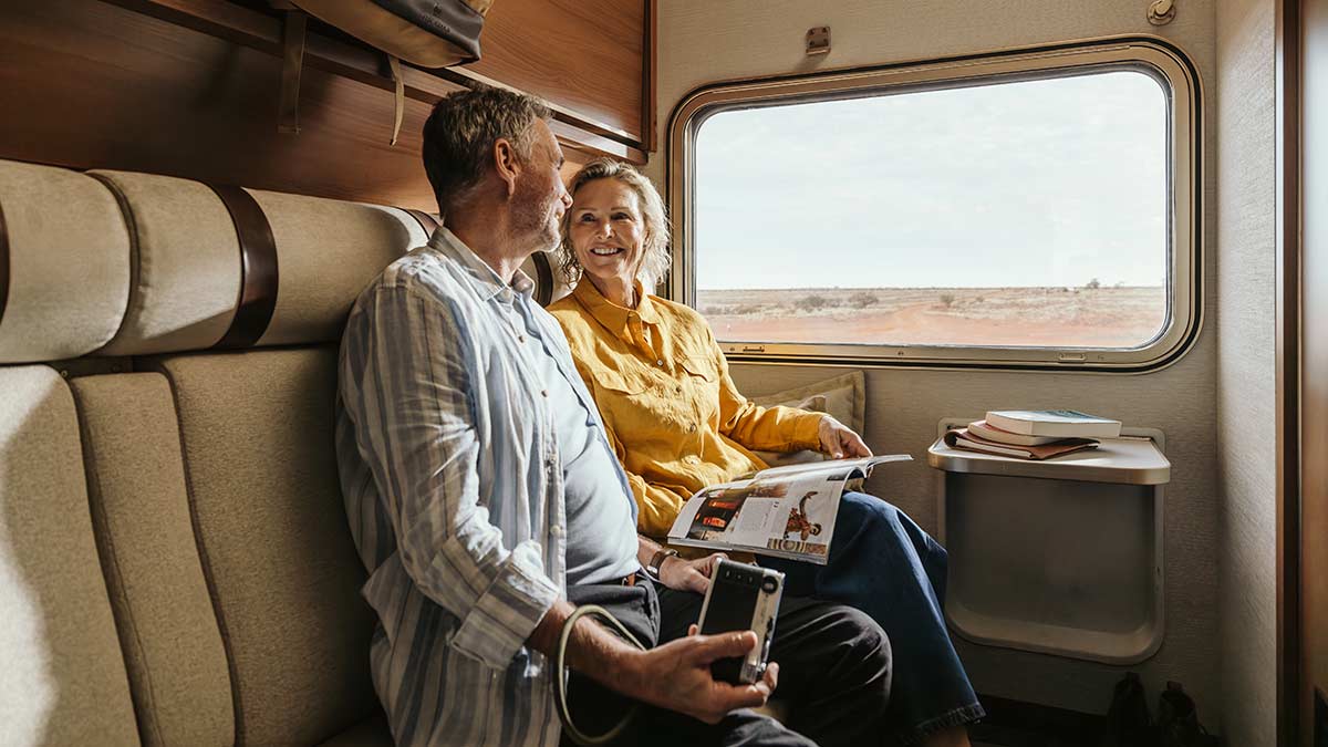 Two people smile as they relax in a Gold Premium Cabin aboard The Ghan train in Australia.