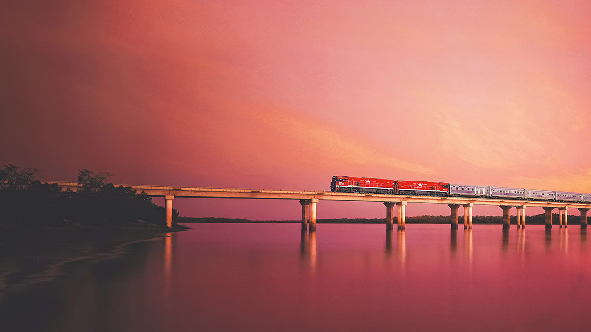 The Ghan train is bathed in red light as it crosses Elizabeth River in the North Territory.