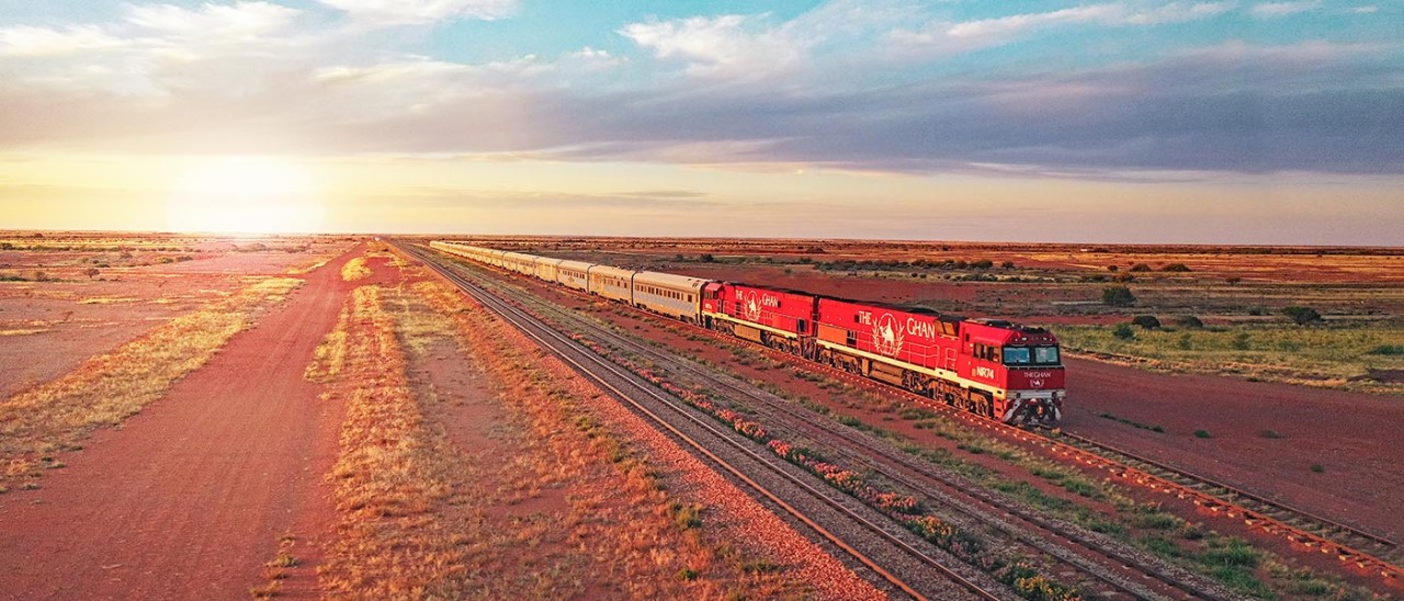 Aerial view of The Ghan surrounded by red earth and the arid, vast landscape of Outback Australia.