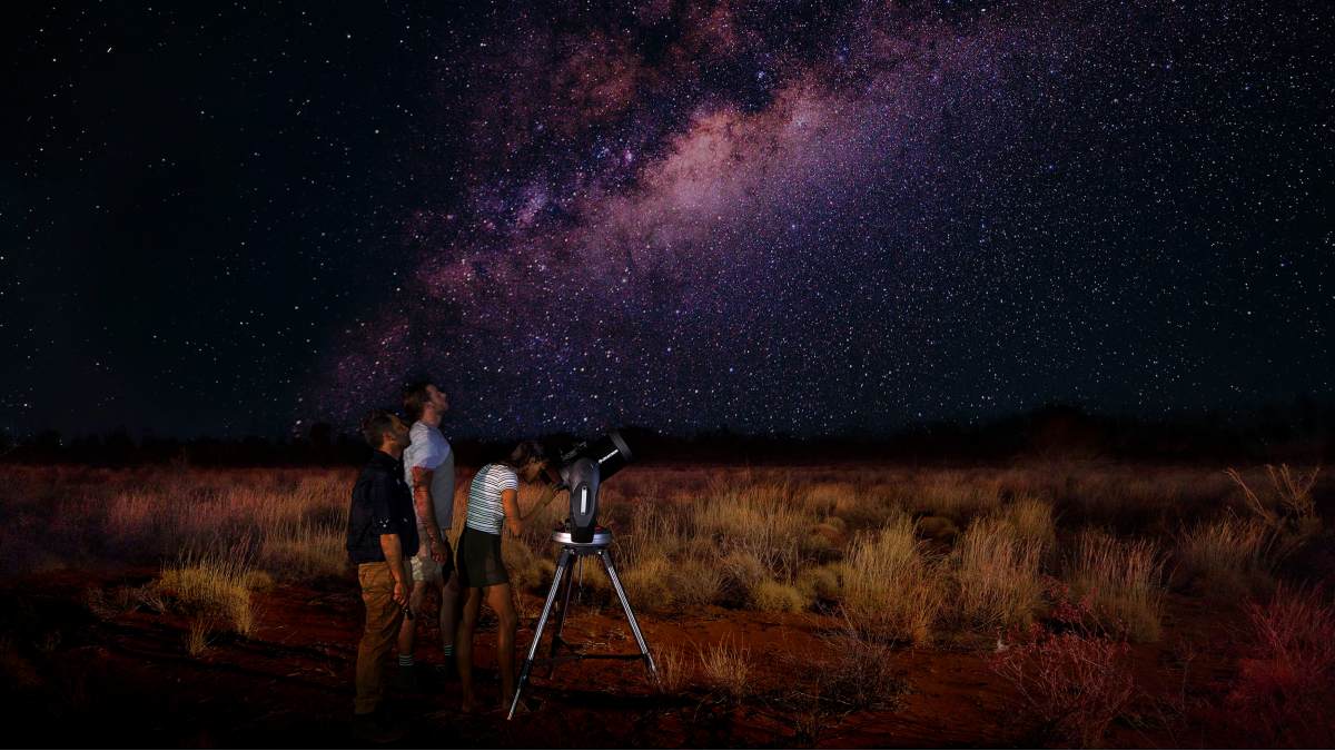 three people using a telescope in the outback at night