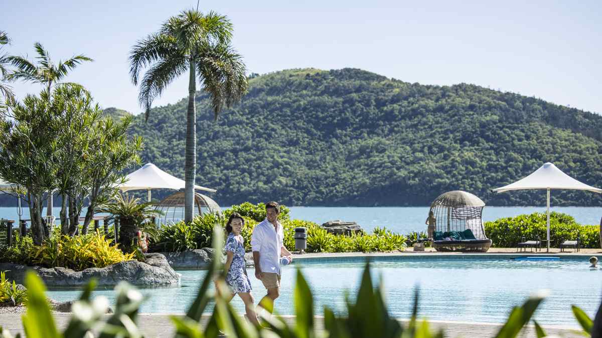 couple walking beside pool at tropical resort