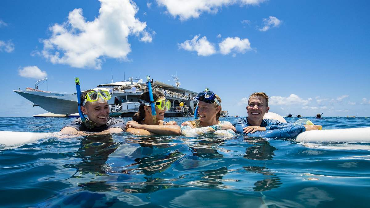 four people snorkelling in ocean with boat in background