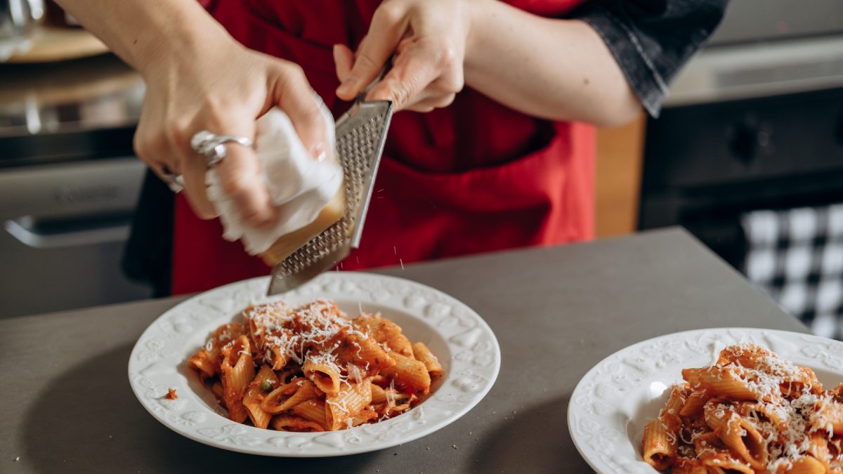 woman shaving cheese over penne pasta