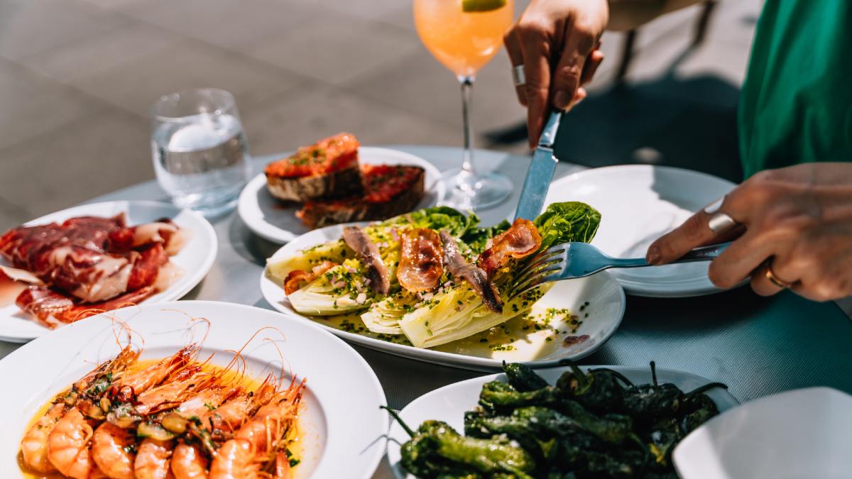 woman eating Spanish tapas including pan con tomate, padron peppers, gambas, iberico ham