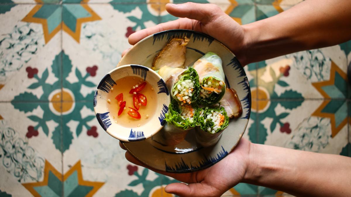 man holding dish with vegetable paper rolls, stewed pork and nuoc cham sauce