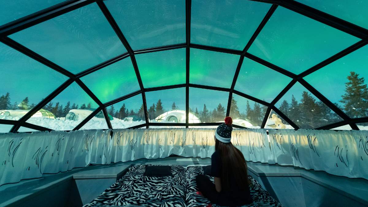woman in glass igloo watching northern lights