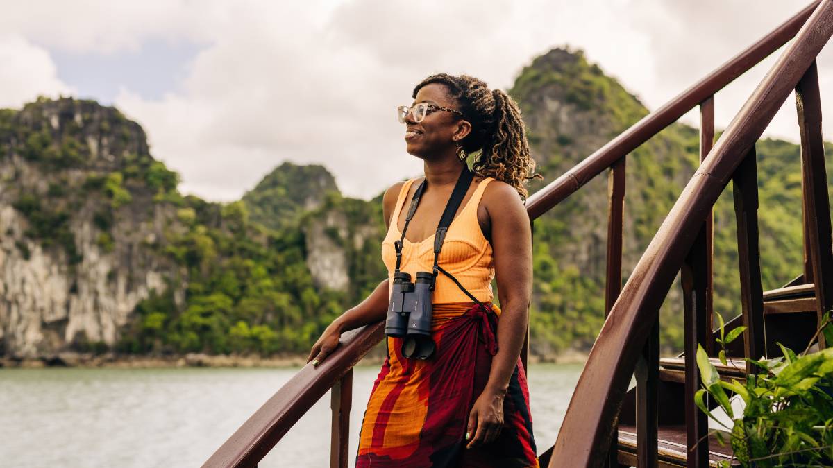 young woman on staircase with binoculars, smiling out at islands