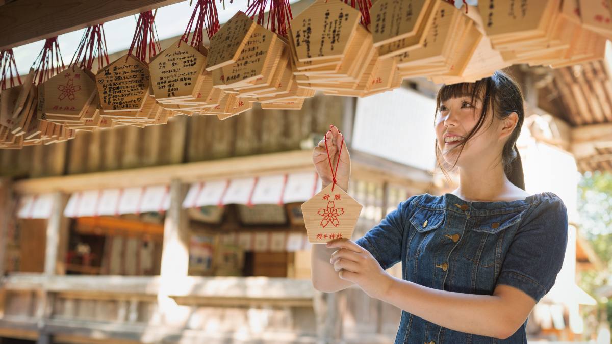 young woman attaching an ema plaque at a shinto shrine