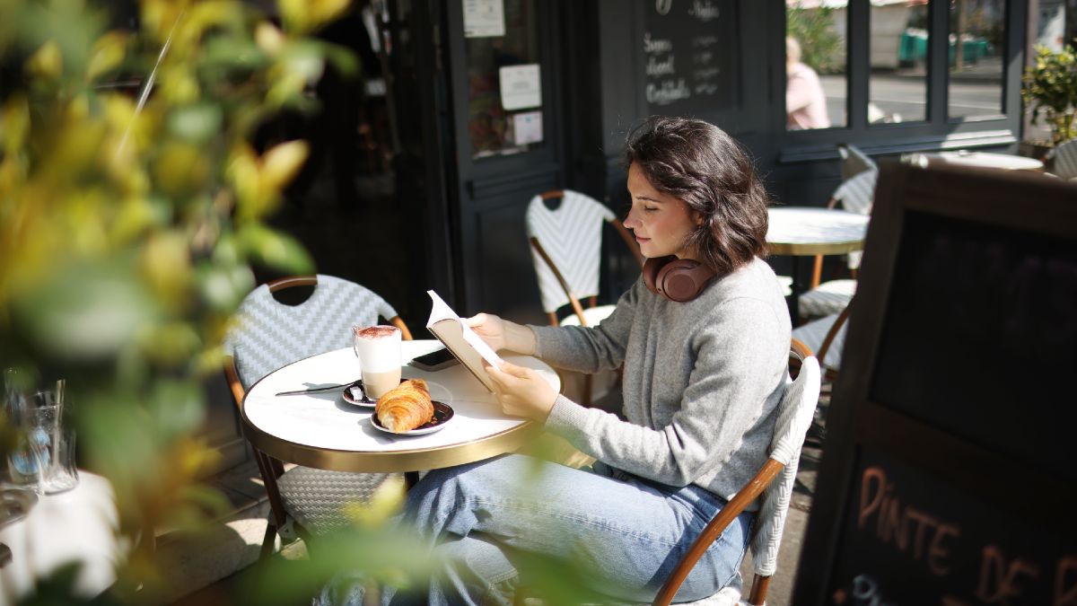 young woman reading at a cafe with a coffee and croissant