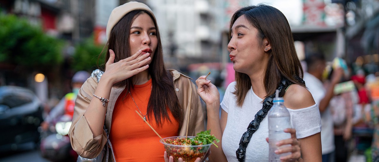 Two women reacting to spicy street food in Thailand