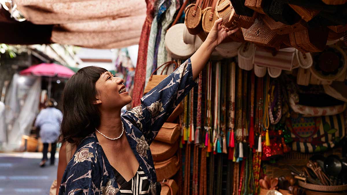 Happy woman reaching at bags hanging at market store in Bali.