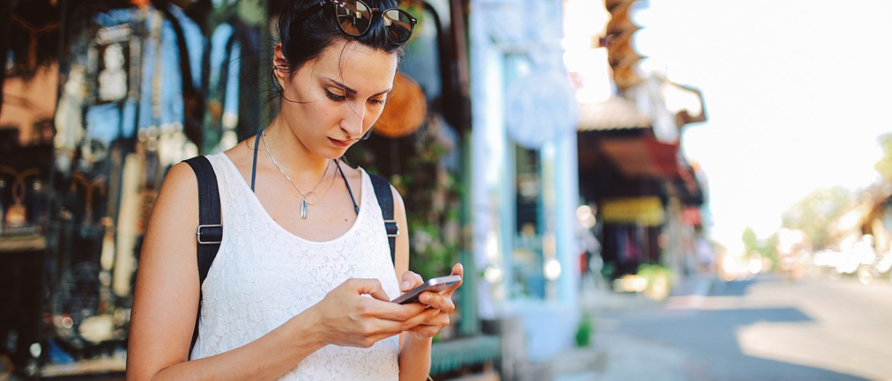 Young woman with a backpack traveling in Bali, Indonesia. She is checking her mobile phone, looking for travel tips on where to go next.