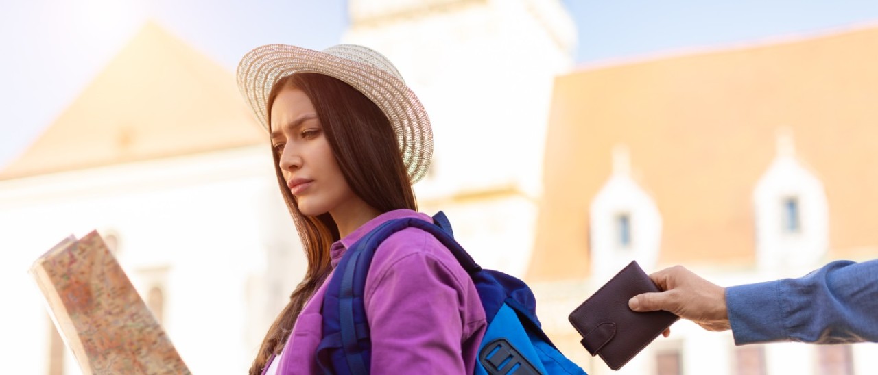 woman in hat and pink jacket reading a map while wallet is stolen by pickpocket from the blue bag on her shoulder