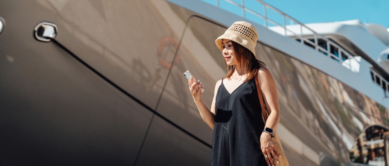 woman smiling at her smartphone as she stands in front of a cruise ship