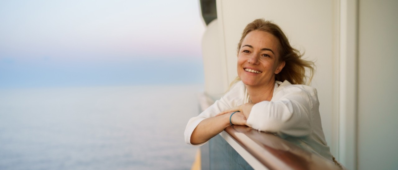 woman leaning on railing of cruise ship smiling