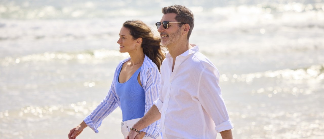 woman and man holding hands and smiling as they walk down a beach