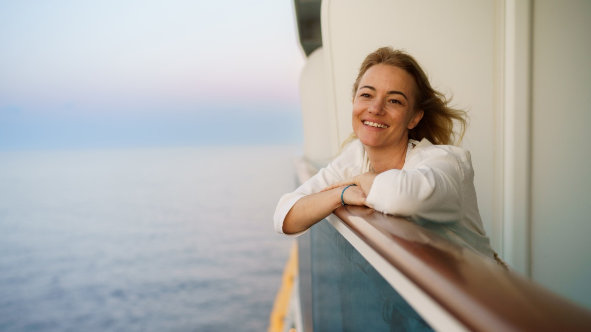 woman leaning on railing of cruise ship smiling