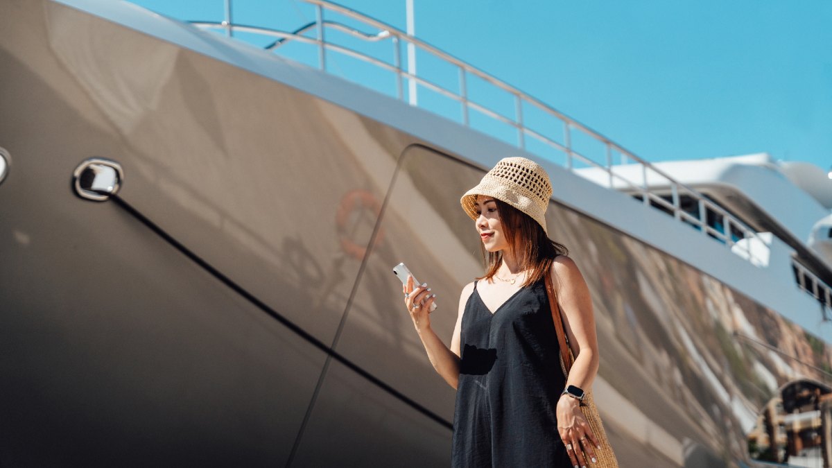 woman smiling at her smartphone as she stands in front of a cruise ship