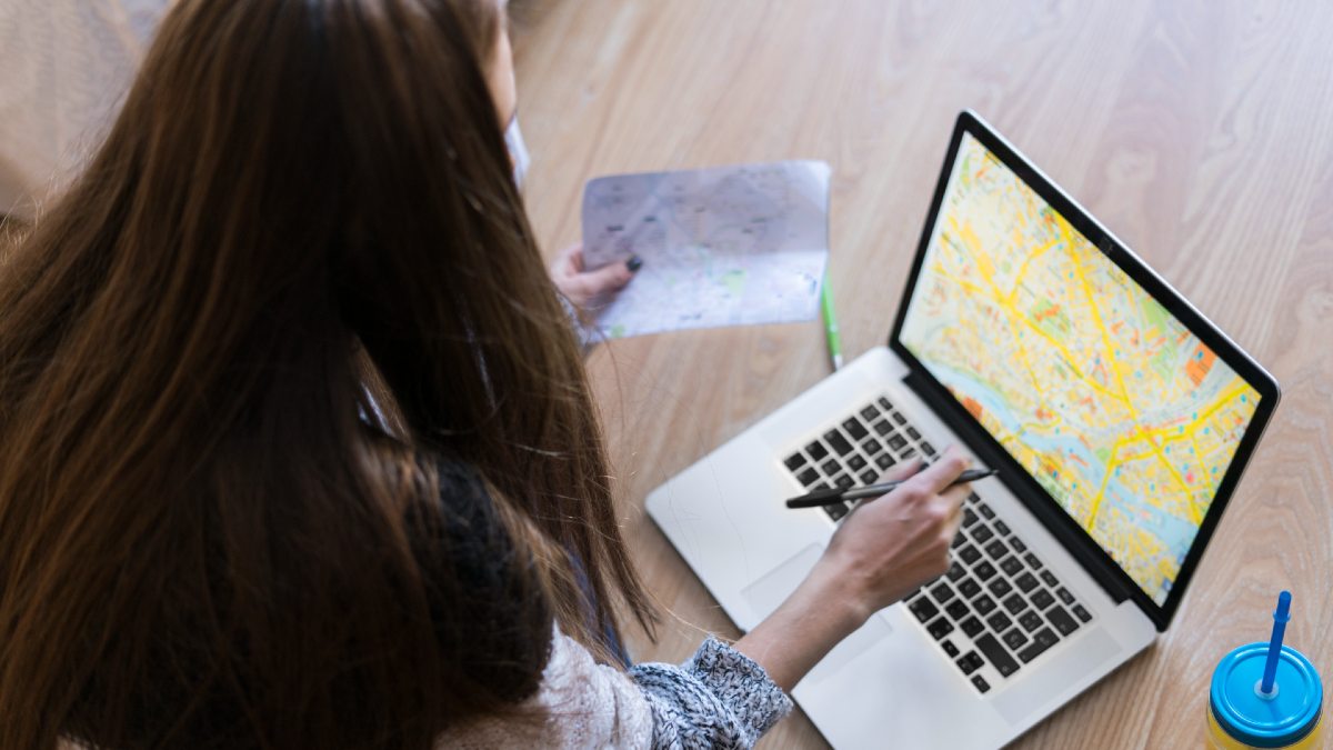 woman researching travel using a laptop and map