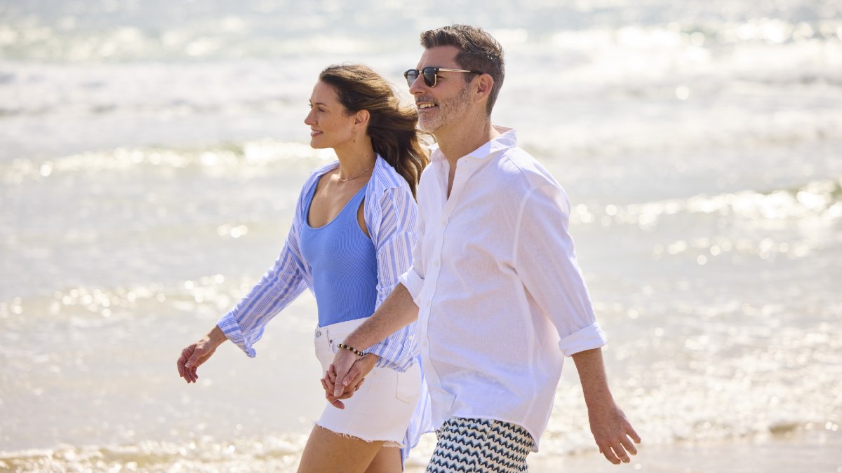 woman and man holding hands and smiling as they walk down a beach