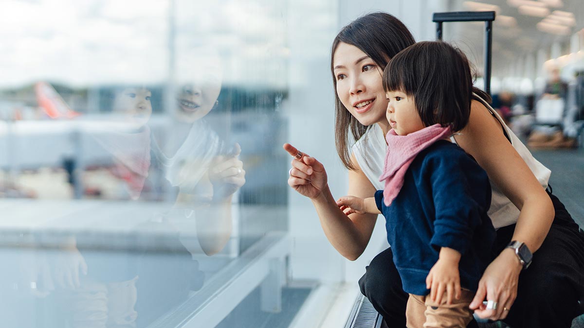 Mother with child pointing to planes outside airport lounge window