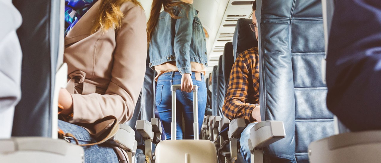 Woman walking down plane aisle wheeling luggage