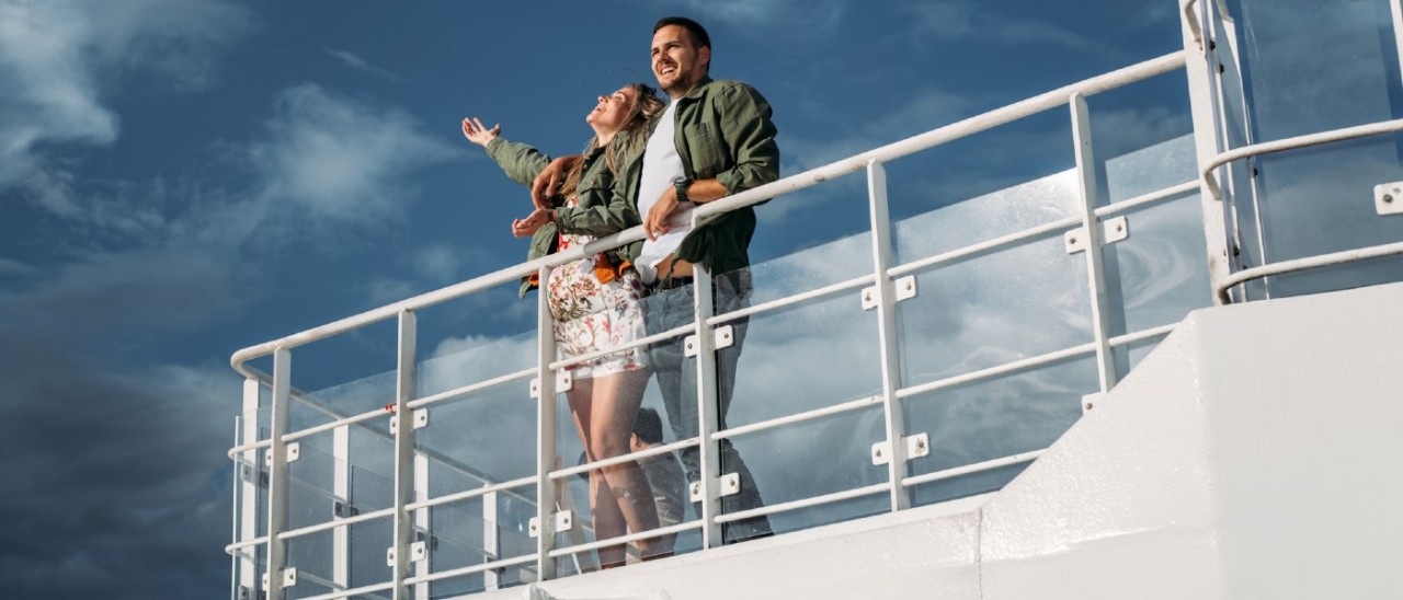man and pregnant woman on upper level of cruise ship smiling