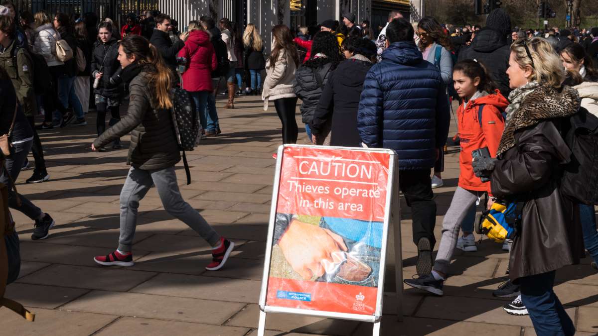 large group of people in public square; notice sign reads CUATION Thieves operate in this area