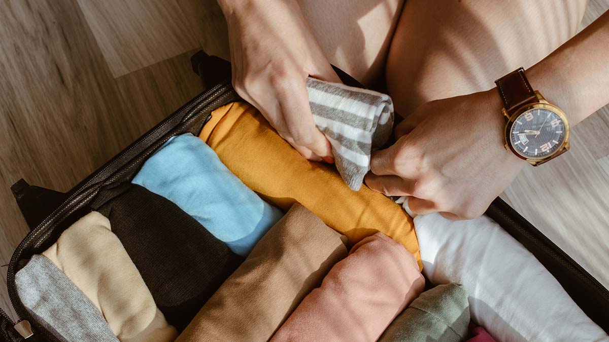 Overhead shot of person rolling clothing and packing suitcase neatly.