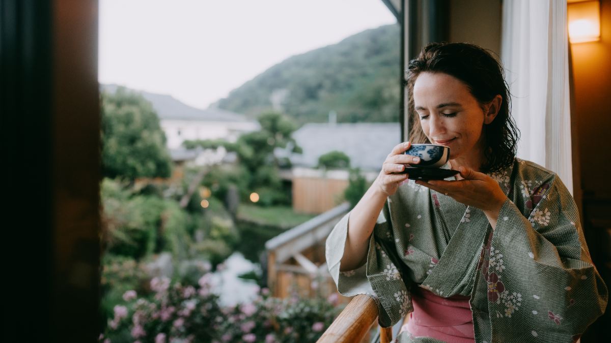 woman wearing kimono drinking tea on balcony overlooking gardens