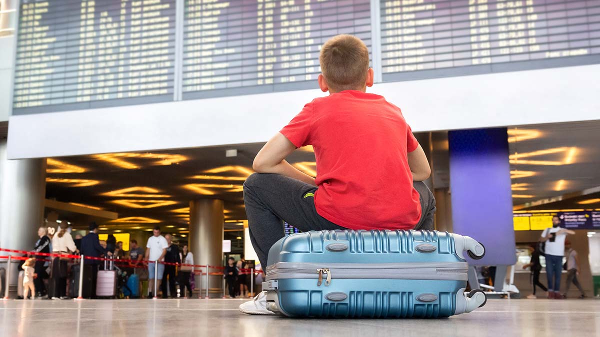 boy sitting on suitcase in airport looking up at departures board