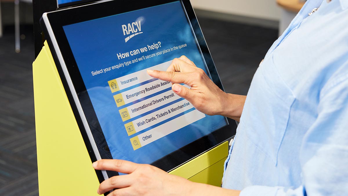 Person using RACV retail store self-service kiosk with finger hovering over the word insurance.