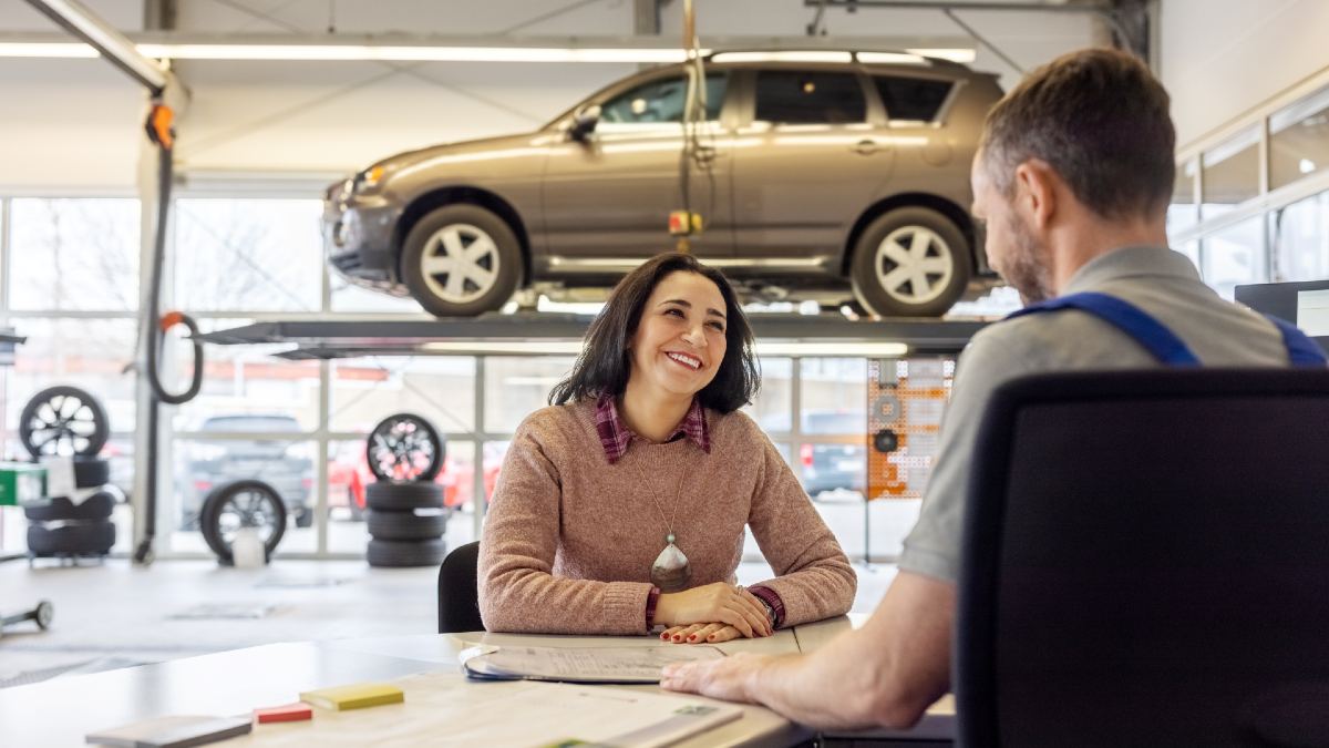 car mechanic speaking to car owner in workshop with elevated car in background
