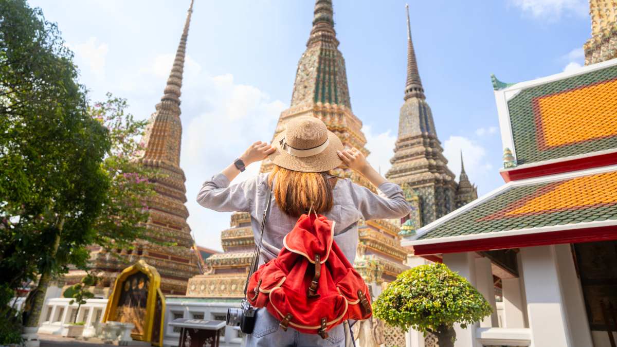 female tourist wearing a hat and backpack looking up at a temple