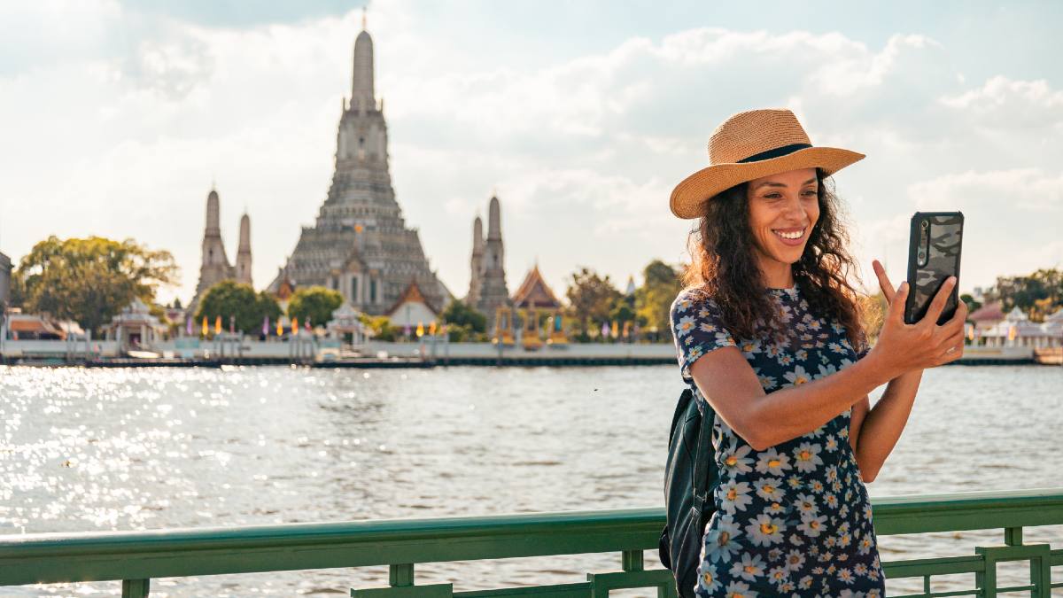 female tourist taking a selfie in front of water and a temple