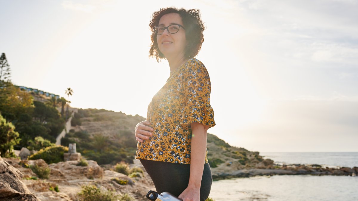 pregnant woman touching her belly as she stands on a beach