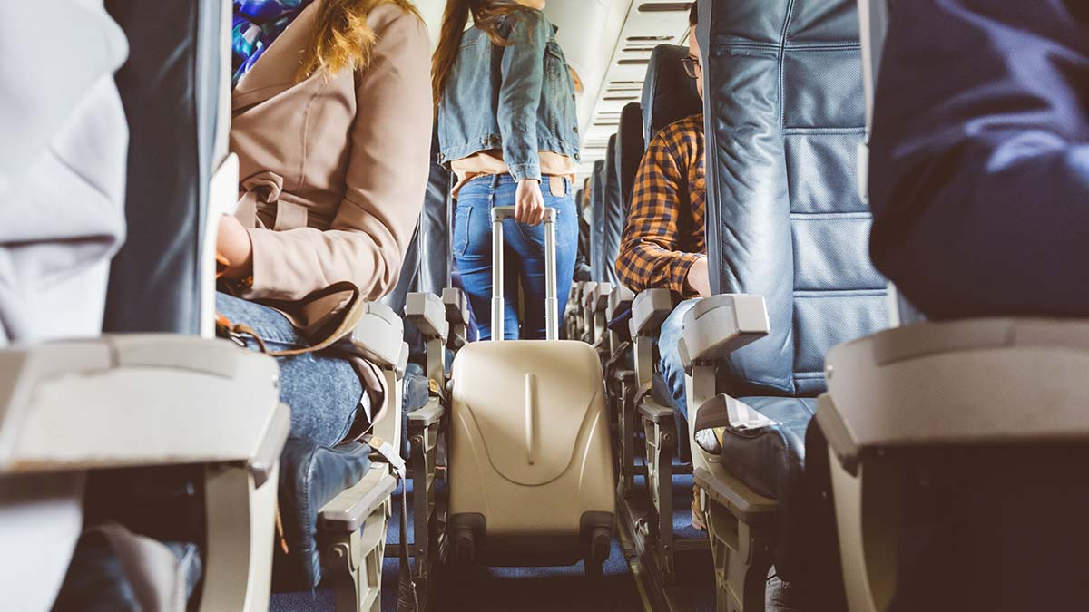 Woman walking down plane aisle wheeling luggage