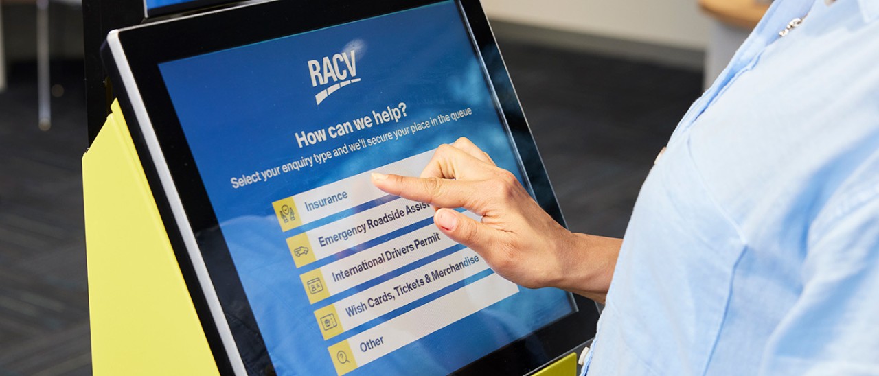 Person using RACV retail store self-service kiosk with finger hovering over the word insurance.