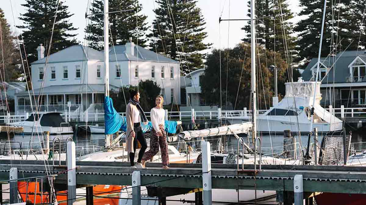 Two women walking along wharf and past boats in Port Fairy.