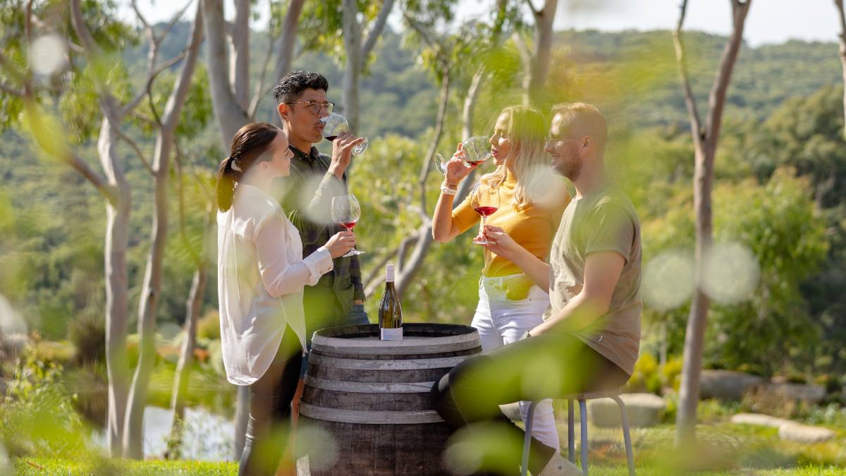 four friends sip wine around a barrel outside