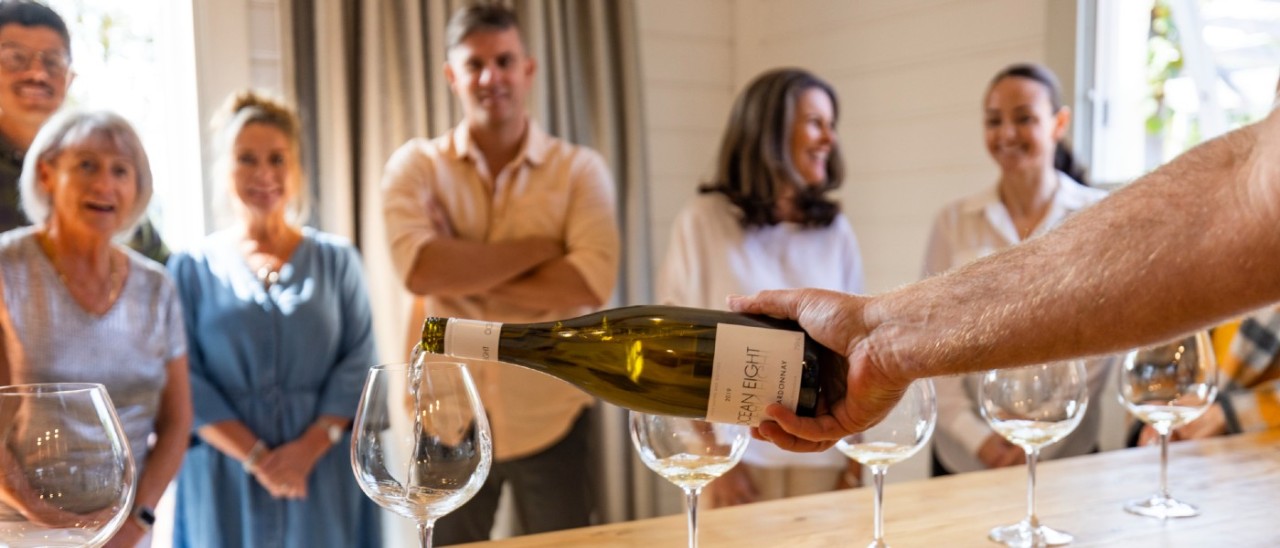 six guests watch a man pour wine