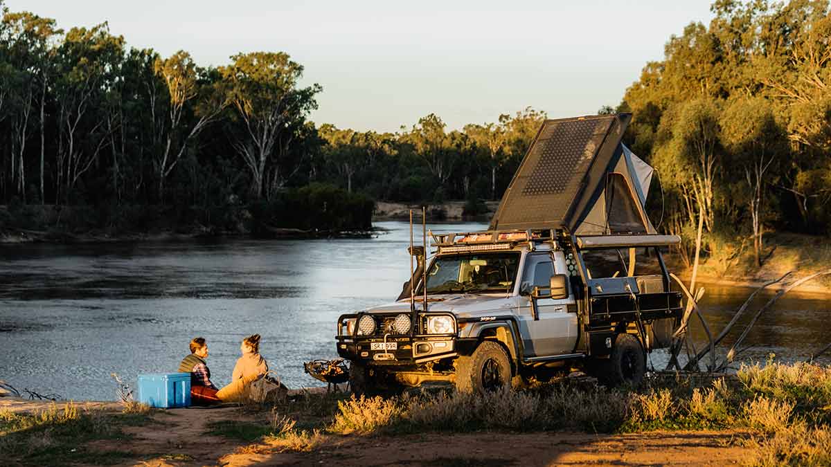 Couple next to campervan enjoying a picnic on river beach