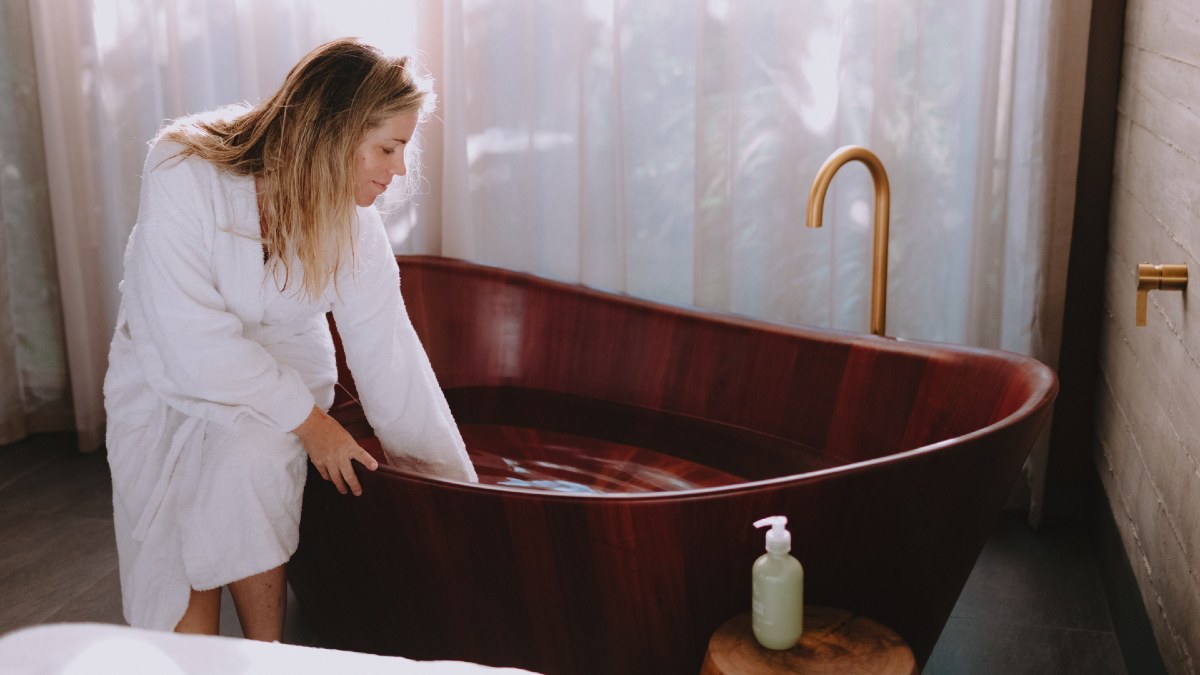 woman in bathrobe checking temperature of bath water at day spa