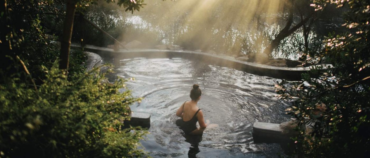 young woman bathing in hot springs surrounded by trees and sunlight