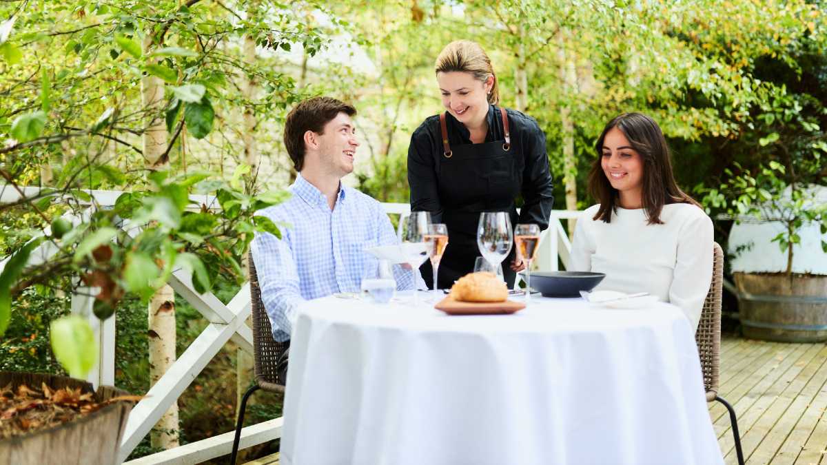 young couple eating at an outdoor table with a waitress serving them